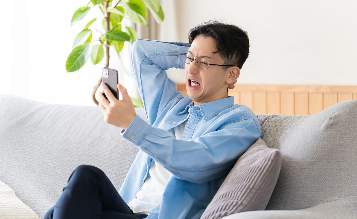 スマートフォンを見て頭を抱える男性